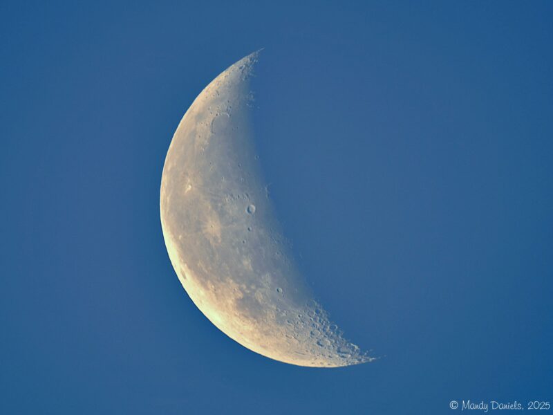 A beautifully illuminated crescent moon, set against a blue sky.