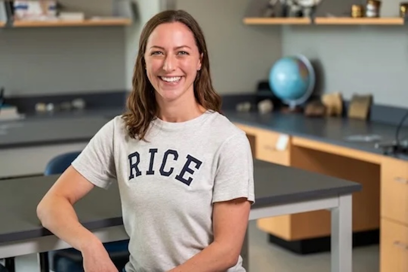 Smiling woman with long hair in a classroom, wearing a white t-shirt that says RICE on it.