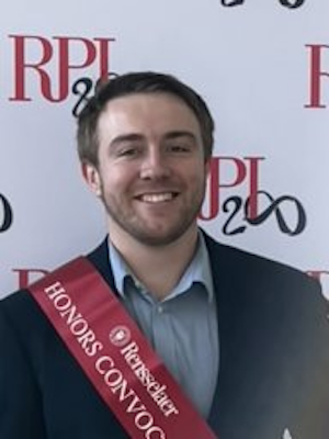 Младић кратке косе и браде, насмејан, са црвеним наградним појасом на грудима.