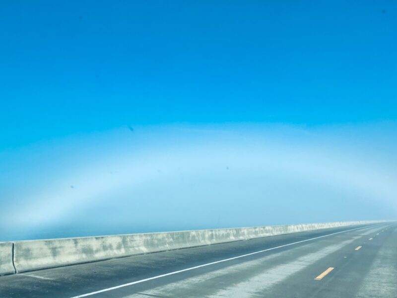 Fuzzy white arc near the horizon in a blue morning sky.
