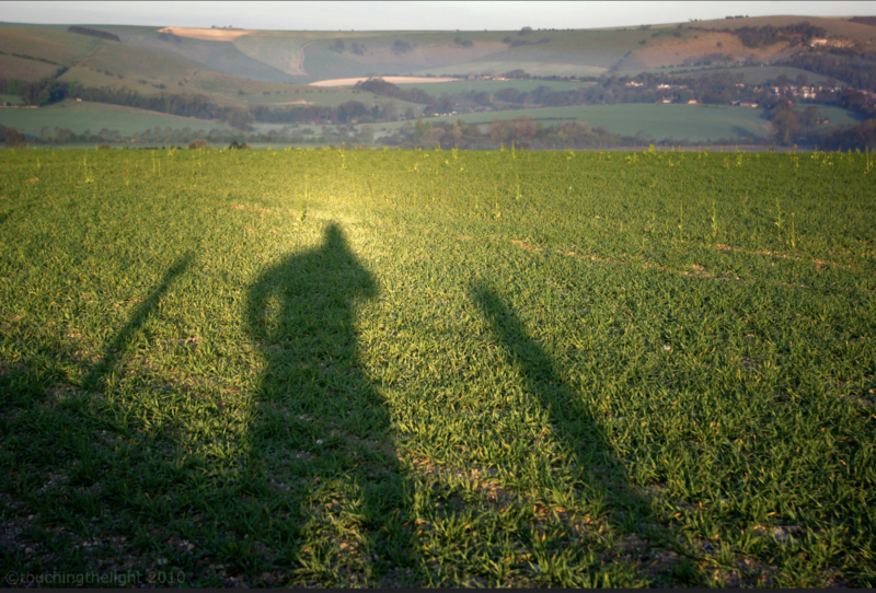 Photo of a broad, green lawn, with the shadow of a man, and a light around his head.