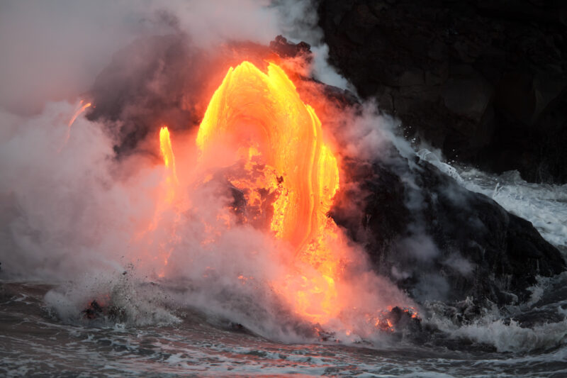 Orange lava flowing into water with steam rising.