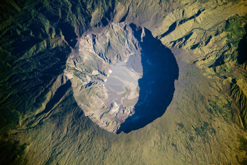 Looking down at a round, rugged crater at the top of a mountain.