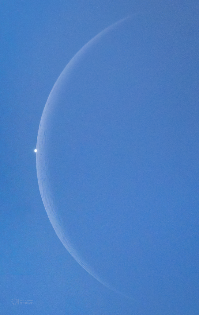 A bright light pokes out from behind the slender edge of the moon.