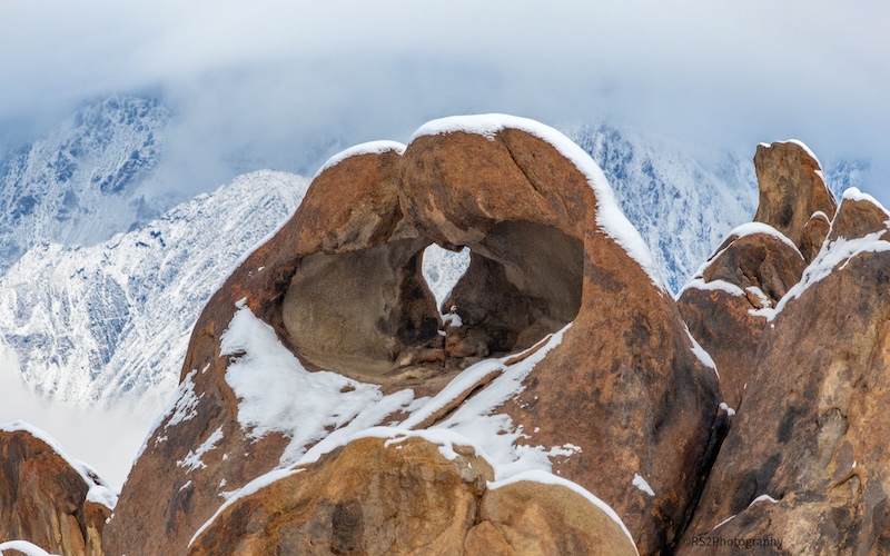 A rock arch among snowy mountains, with the hole in the arch being heart-shaped.