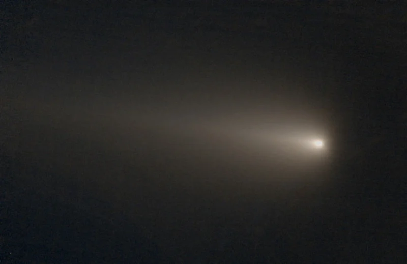 A comet in a black background, with a tail blowing back from the right.