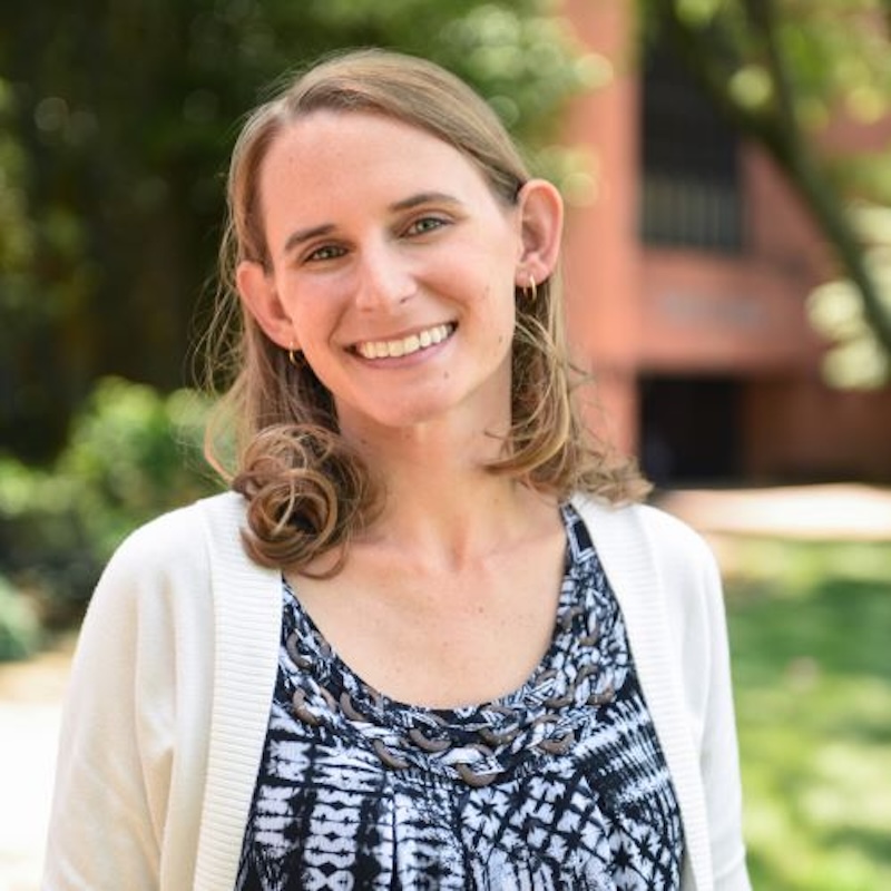 Smiling woman wearing a patterned shirt with a white cardigan on top of it.