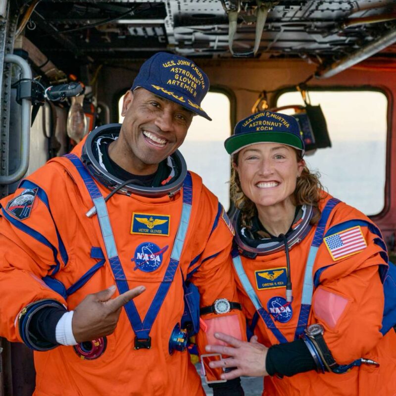 2 smiling people in orange flight suits.