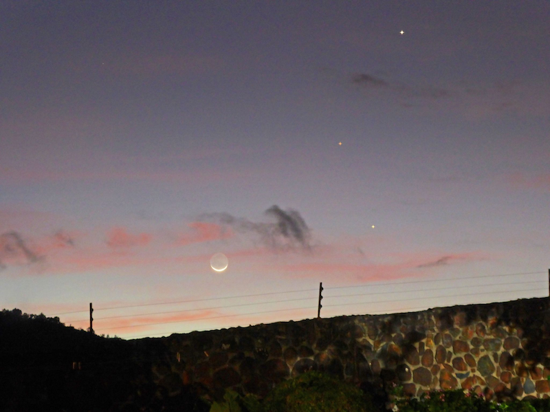 Thin crescent moon near horizon at dawn with 3 dots, 1 extra-bright and 1 reddish.