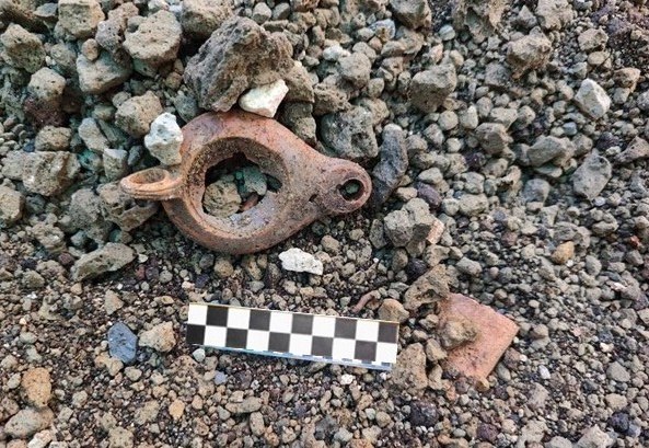 Small, brown clay lamp on gravel surface with a black and white scale ruler.