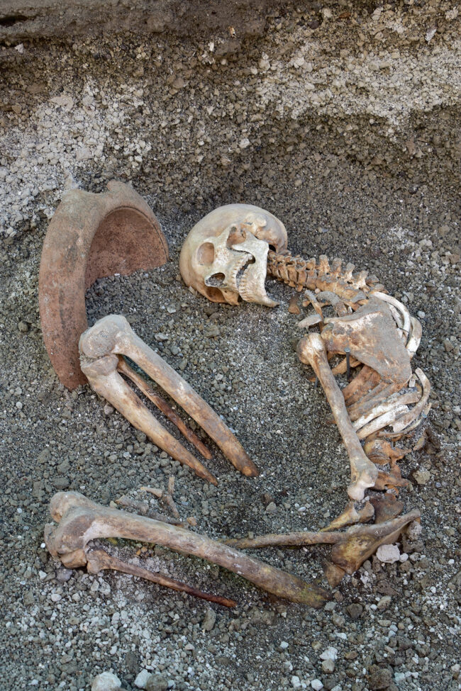 Skeleton curled up with a large terracotta bowl with a fracture missing near its head.