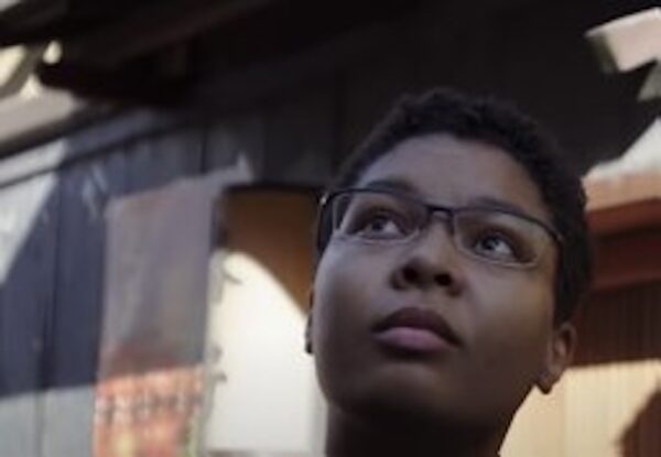 Dark complexioned woman with eyeglasses looking upward.