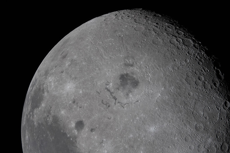 The moon showing a large impact crater centered and many smaller craters near the terminator at upper right.