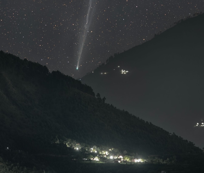 A bright, green dot with a long, gray tail between the mountains.