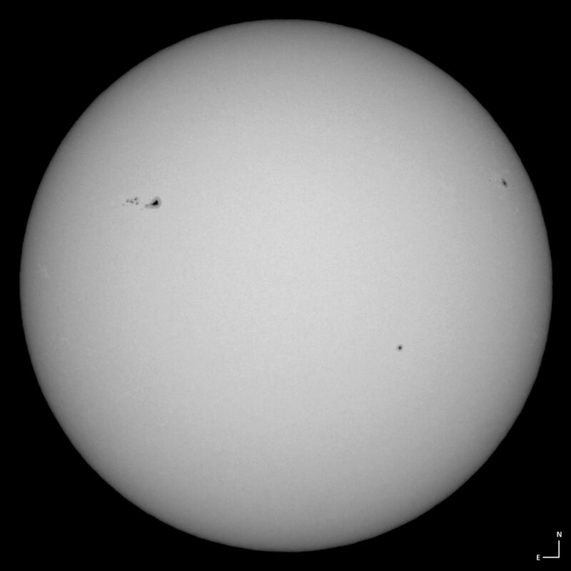 The sun, seen as a large white sphere with small dark spots.