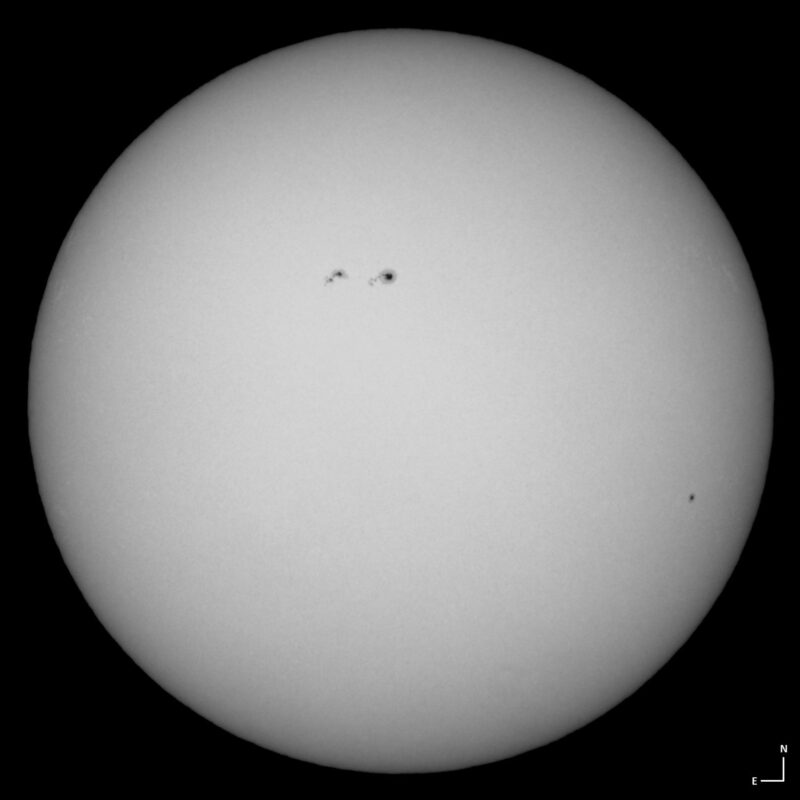 The sun, seen as a large white sphere with small dark spots.