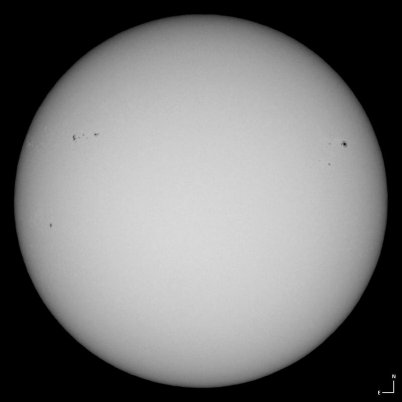The sun, seen as a large white sphere with small dark spots.