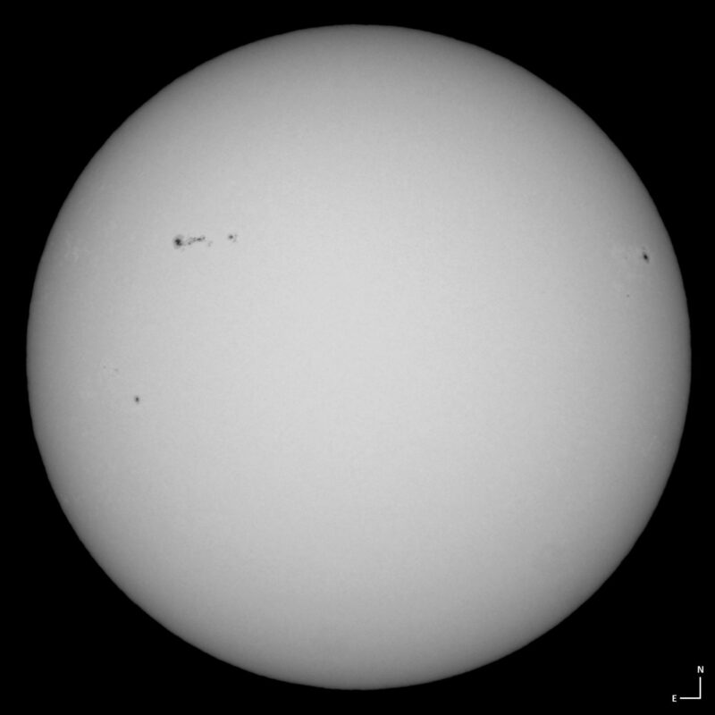 The sun, seen as a large white sphere with small dark spots.