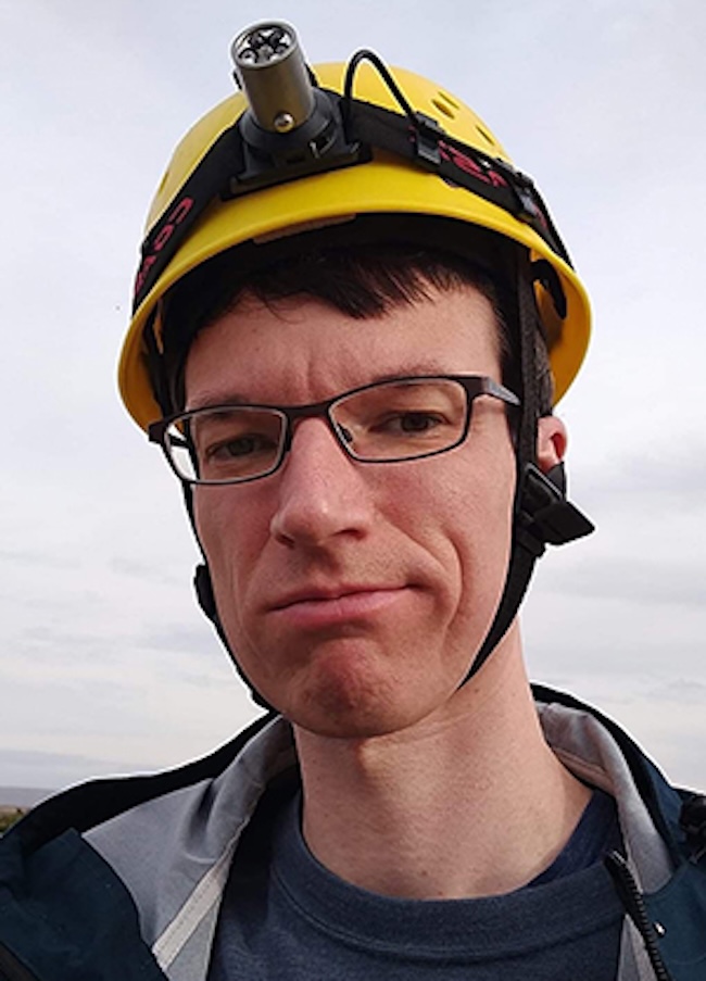 Smirking man wearing a yellow safety helmet.