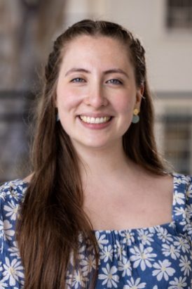 A light-skinned woman with long hair wearing a blue blouse with white flowers.