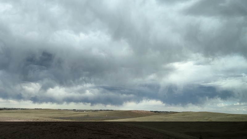 Prairie land in the distance, gray streamers of virga coming down against the distant sky.