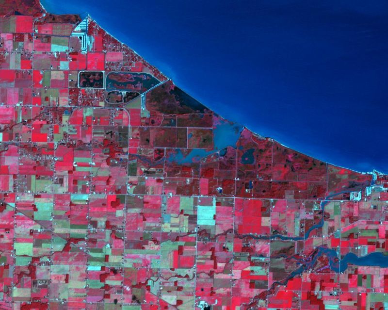 Orbital view of landscape divided into many small rectangles in various shades of red, next to a body of water.