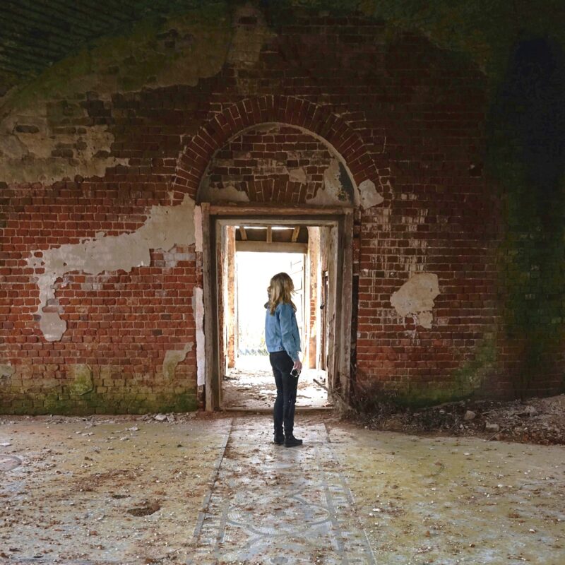 Paranormal experiences: Woman standing inside an old, decrepit abandoned building, looking up toward a high ceiling.