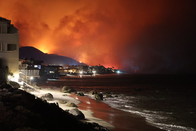 Western US wildfires: Houses on the Pacific Coast with a glow of orange fire in the sky behind.