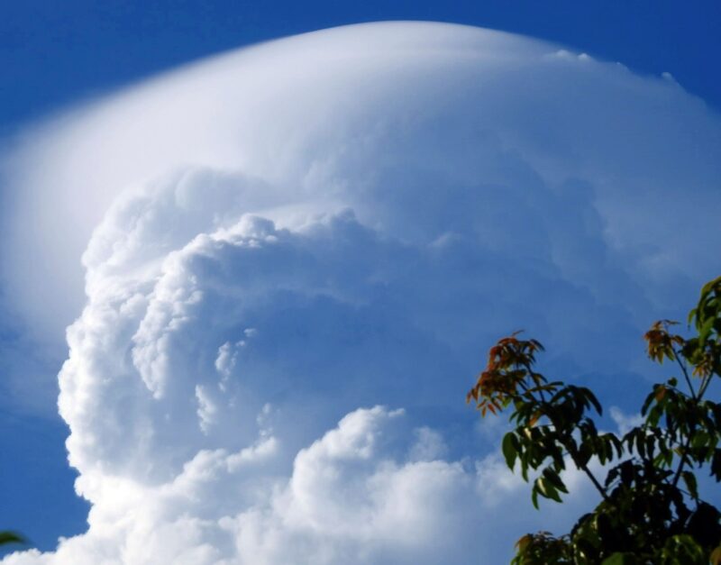 Thick, curved, amorphous white cloud on top of a towering cumulus.