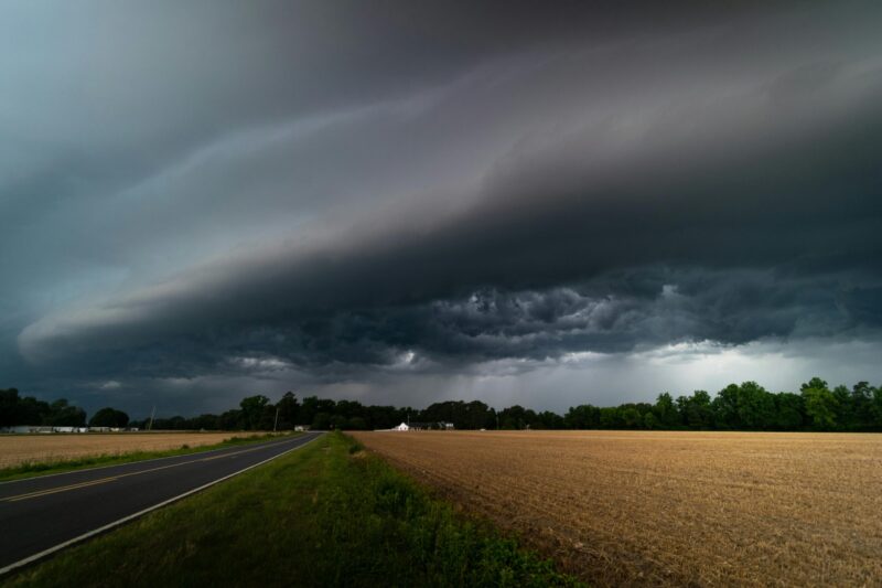 Very dark wall of clouds and distant rain over a farm landscape with a road.