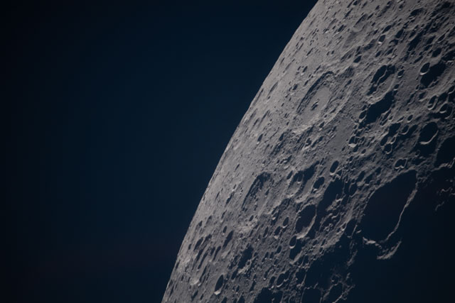 Part of the moon seen against black space. It is heavily cratered.