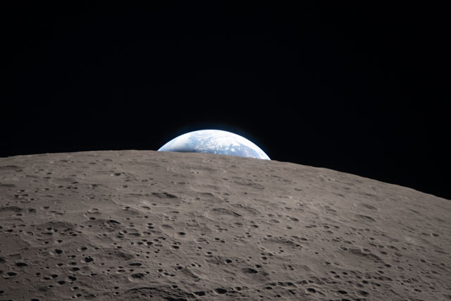 Blue smidge of Earth peeking over limb of cratered moon.
