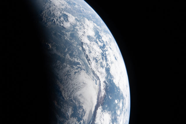 Part of Earth showing blue water and white clouds plus a little land below.