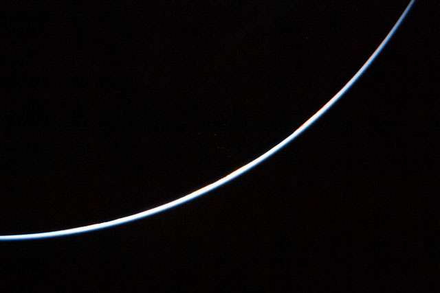 Thin light blue curve, brighter in the middle, through darkness.