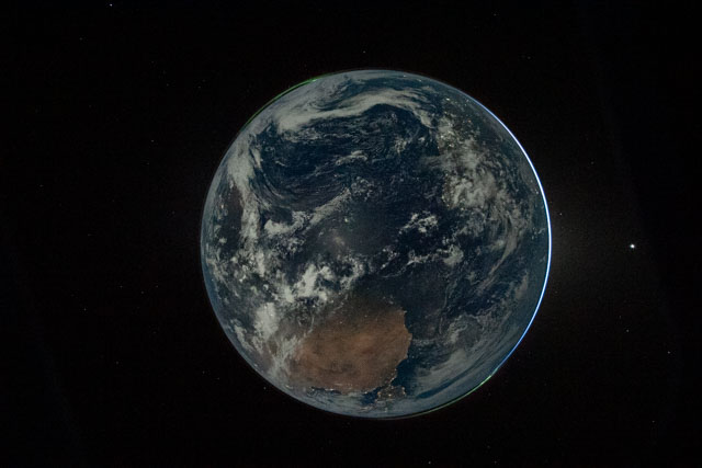 A darkish blue and gray Earth with a sliver of light on the right side.