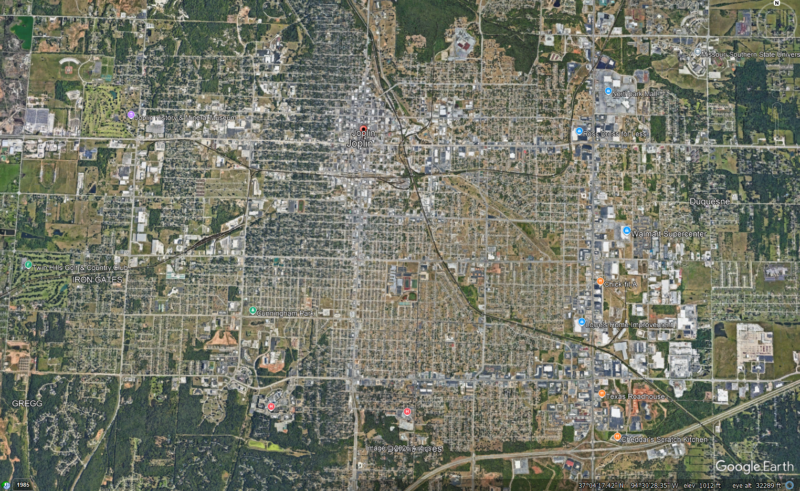 Satellite view of a city with roads and dark green trees plus a lighter tan strip.