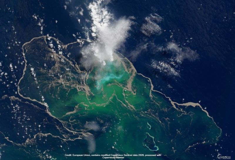 Satellite view of sea, with green area outlined with tan lines, and a few large streamers of steam from one end.
