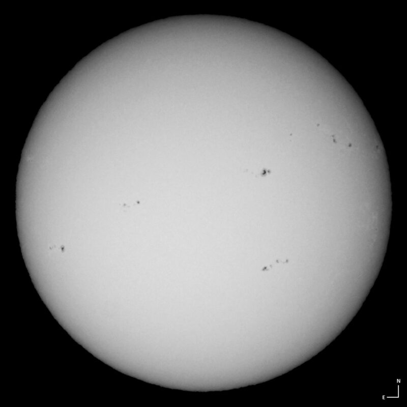 The sun, seen as a large white sphere with small dark spots.