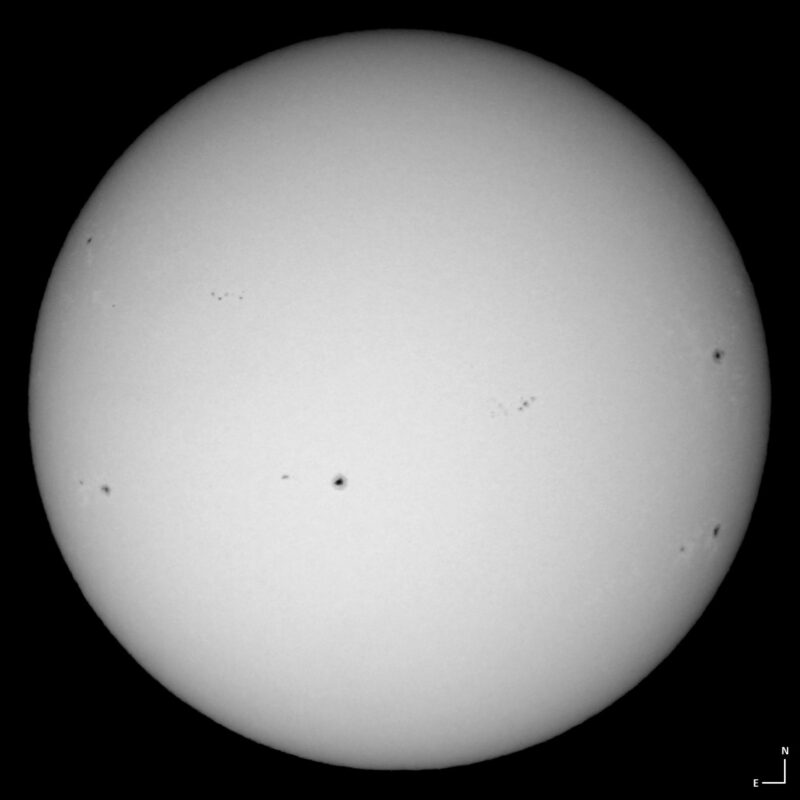 The sun, seen as a large white sphere with small dark spots.