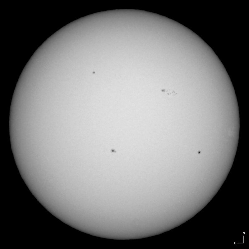 The sun, seen as a large white sphere with small dark spots.