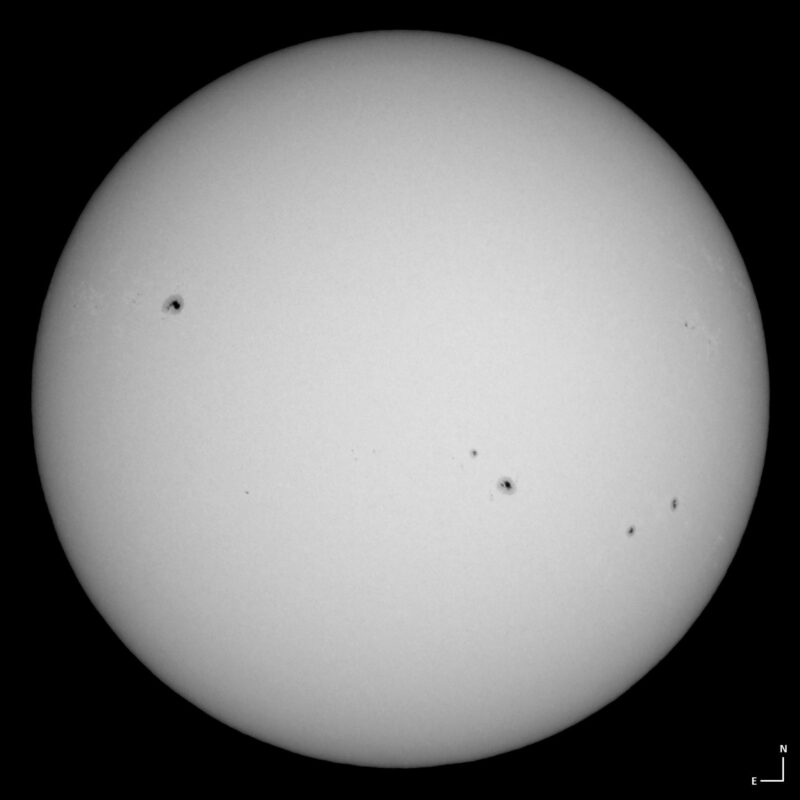 The sun, seen as a large white sphere with small dark spots.