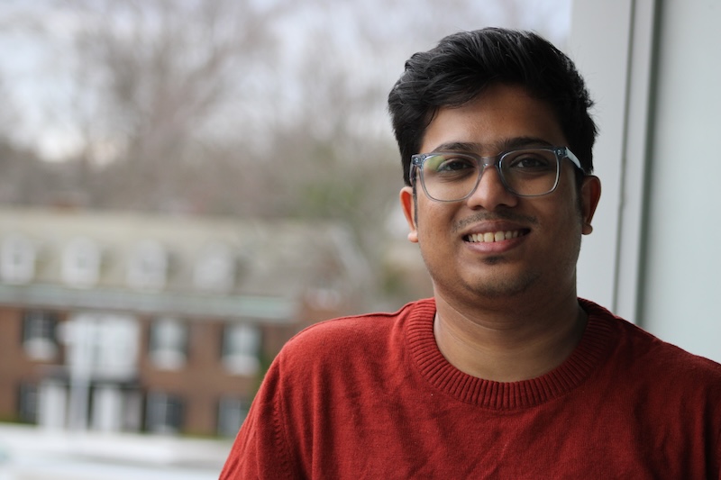 Smiling young man with short black hair wearing eyeglasses and a red sweater.