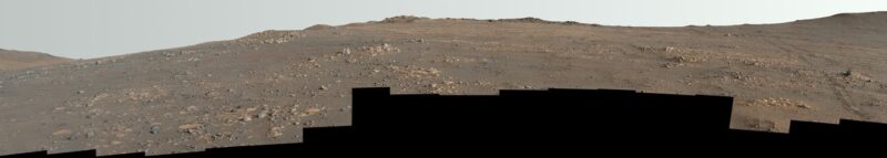 Long narrow panoraman image showing brown and tan rocky landscape under a light sky.