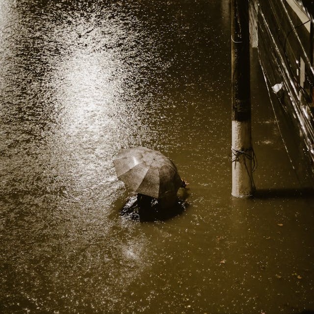 View from above of someone with an umbrella wading through high water at night under a streetlight.