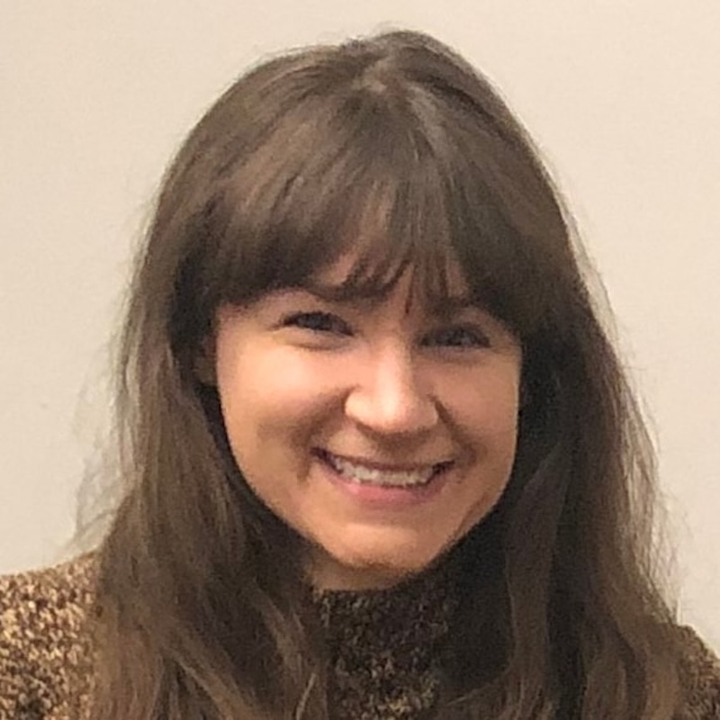 Broadly smiling young woman with long brown hair and bangs.