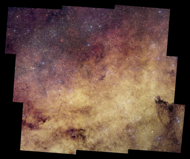 View with irregular edges showing an area packed with stars and some dark nebulae or clouds.