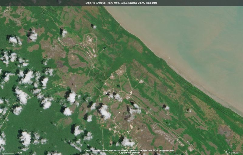 Water at upper right with green land and a couple areas with radial lines on the ground plus clouds.
