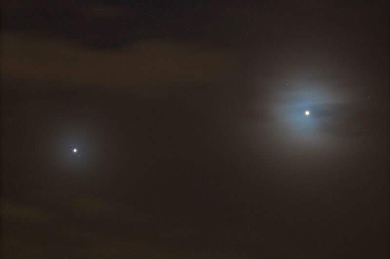 A bright dot with tiny dots in a line next to it, crossing the planet. A brighter dot to its right.