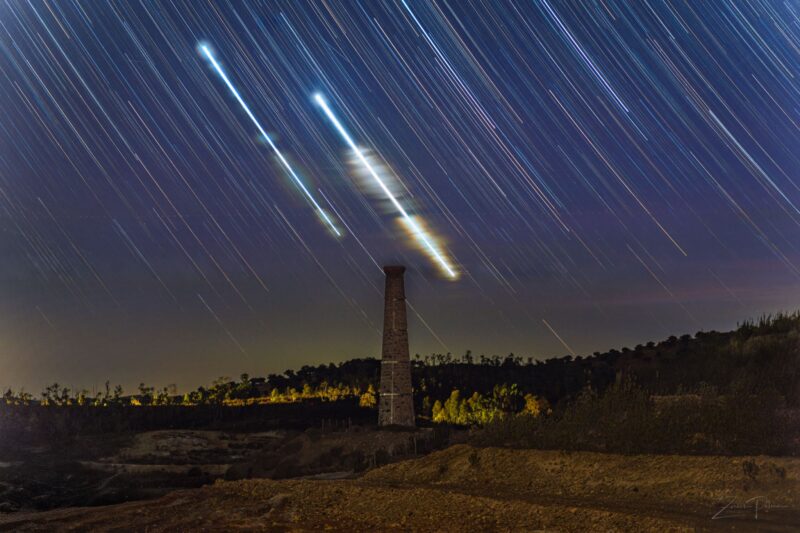 Sky trails with two much brighter than the rest over a dark background and tower.