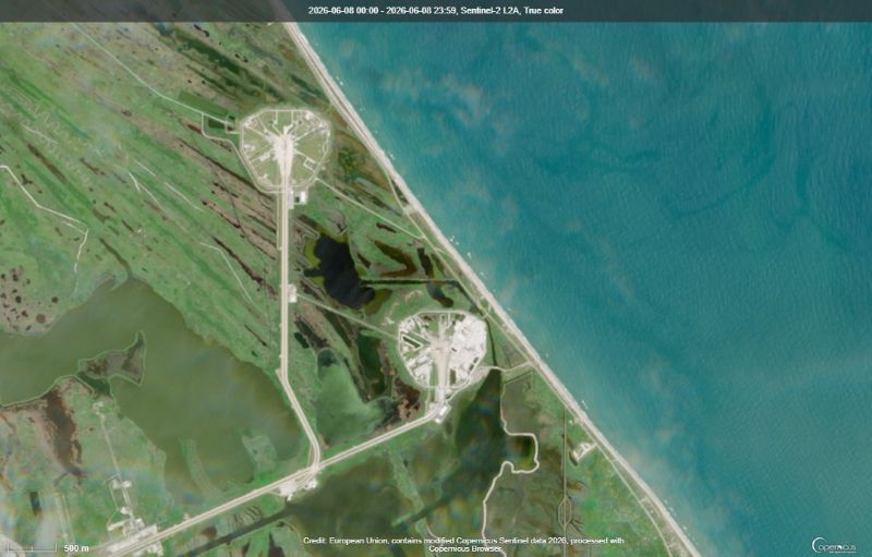 View of water, beach and green land with two round areas with roads leading to them in white.